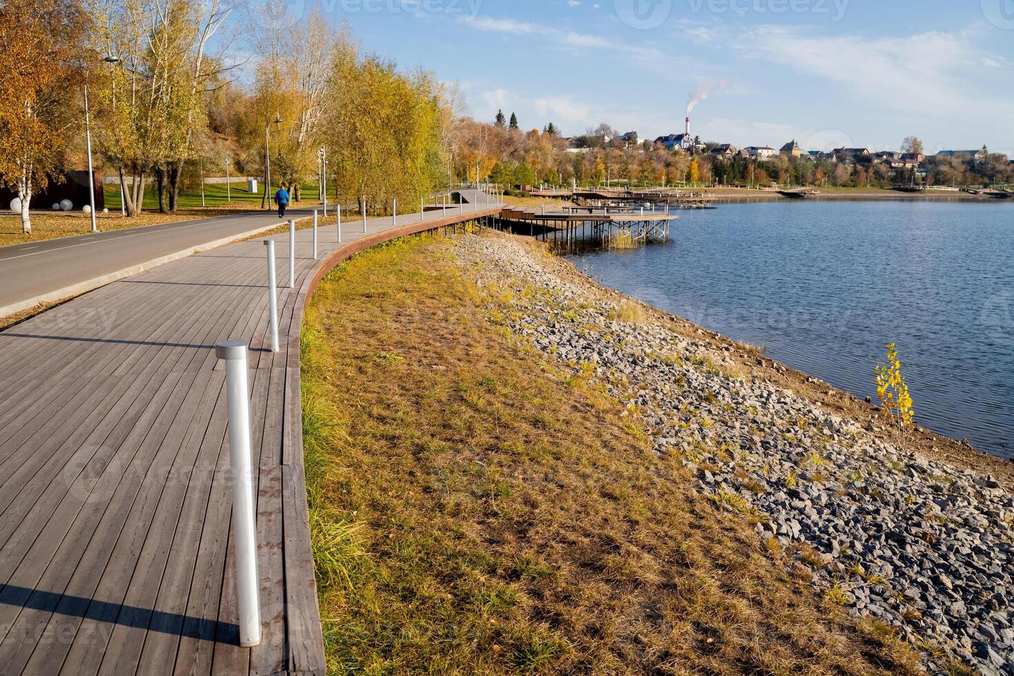 A person leisurely strolls along a lovely wooden walkway that borders a peaceful lake, taking in and appreciating the breathtaking natural beauty that surrounds this tranquil setting photo