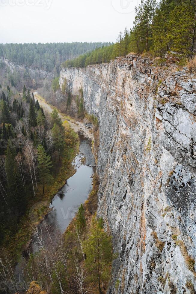 A serene river is gracefully flowing through a picturesque valley, beautifully nestled between two majestic cliffs that are lushly surrounded by vibrant trees and rich greenery all around photo