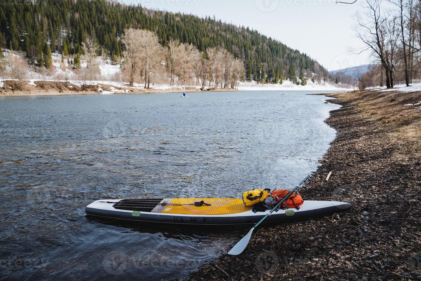 SUP board stands on the bank of a mountain river, extreme rafting with things on a board with a paddle on a lake in the forest, hiking equipment, hiking alone. photo