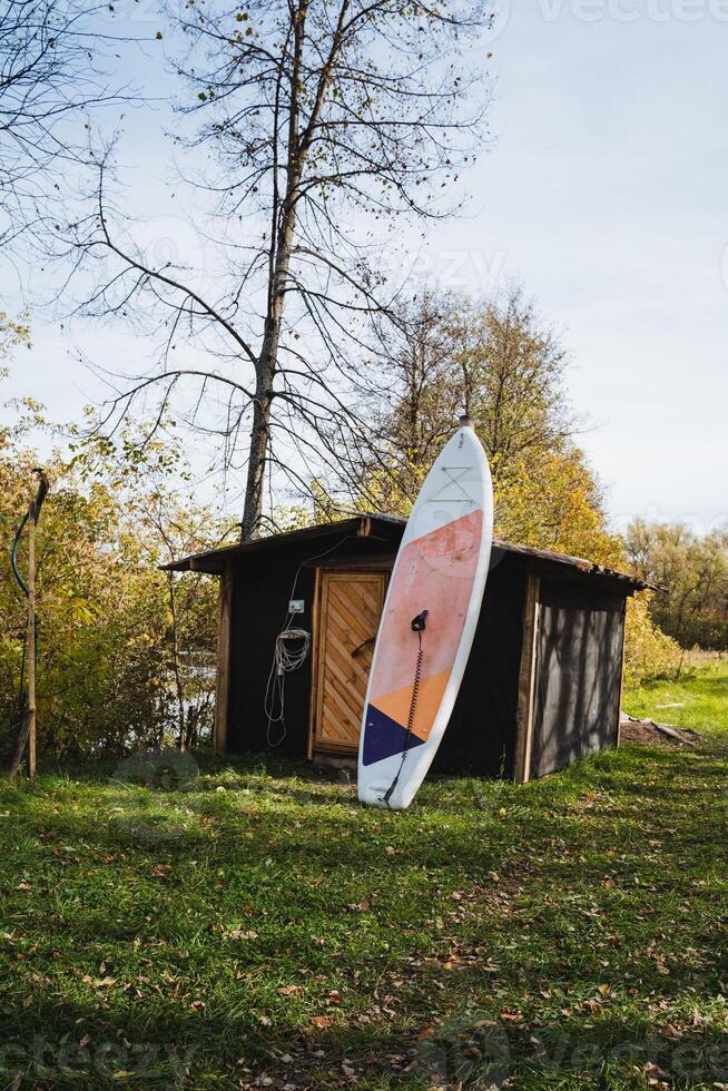In a serene natural landscape, a surfboard is casually leaning against a rustic wooden shed, surrounded by lush green grass, capturing the essence of a laidback outdoor atmosphere photo