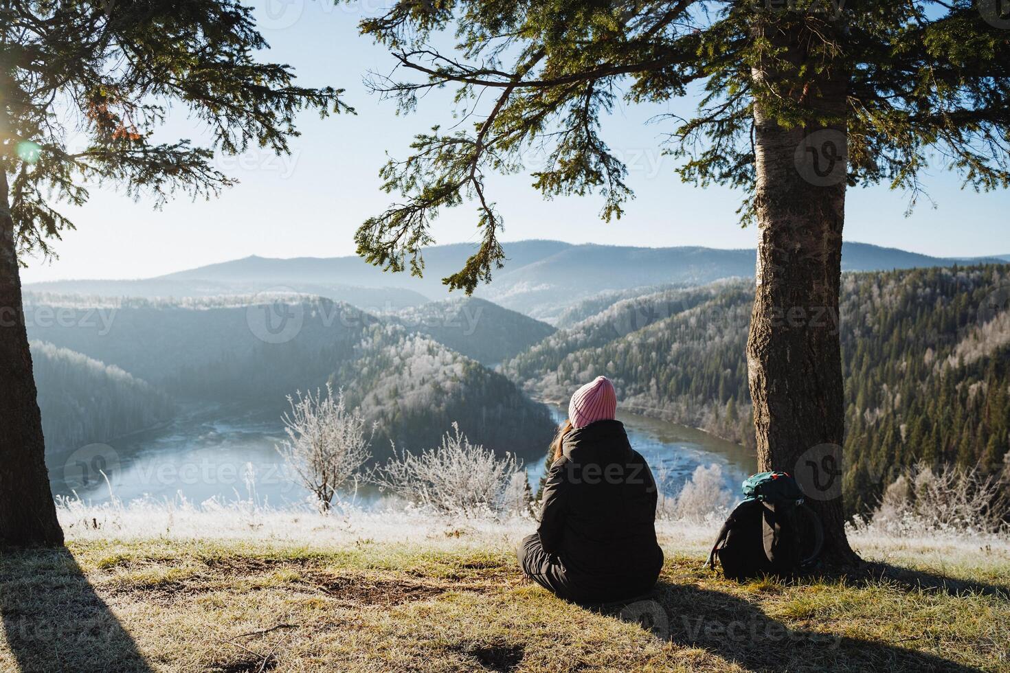 The girl is sitting on the ground and looking at the beautiful winter landscape, traveling in the mountains, time for meditation and yoga practice, relaxing in silence, peace. photo
