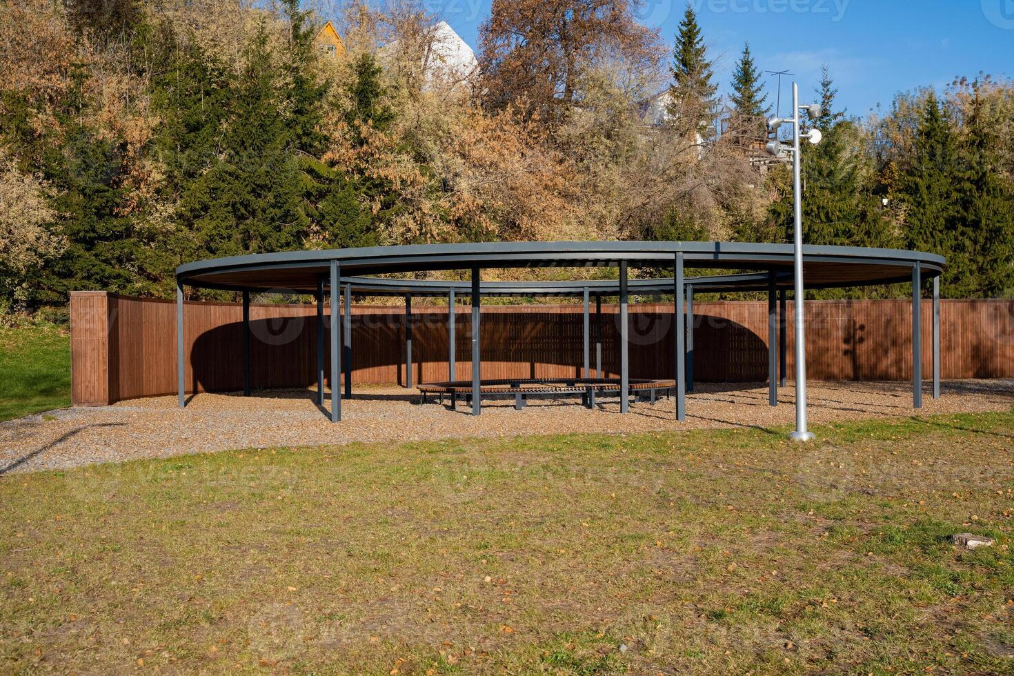 A designated covered area located within a park, featuring several trees in the background that enhance the natural beauty of the surroundings and provide a tranquil environment photo