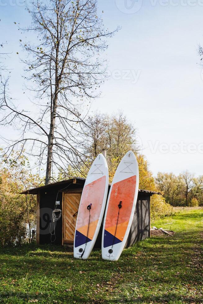 Two vibrant surfboards are leaning casually against a wooden shed, surrounded by lush green grass, creating a relaxed atmosphere perfect for a day of beachside fun and enjoyment photo