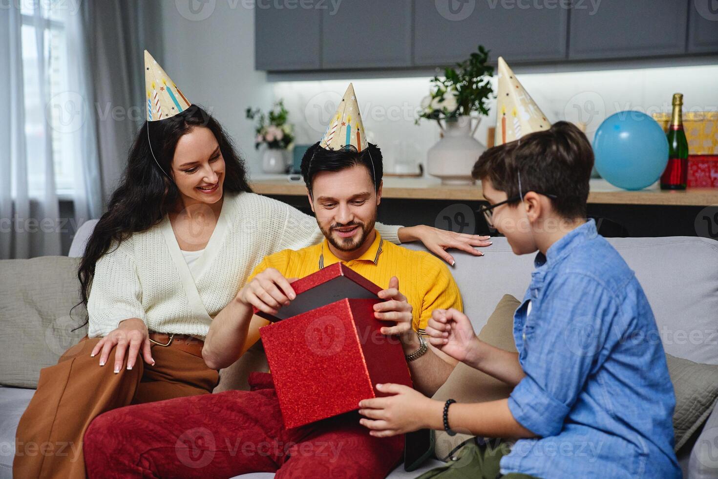 Family celebrates a birthday with gifts and party hats in a cozy living room photo