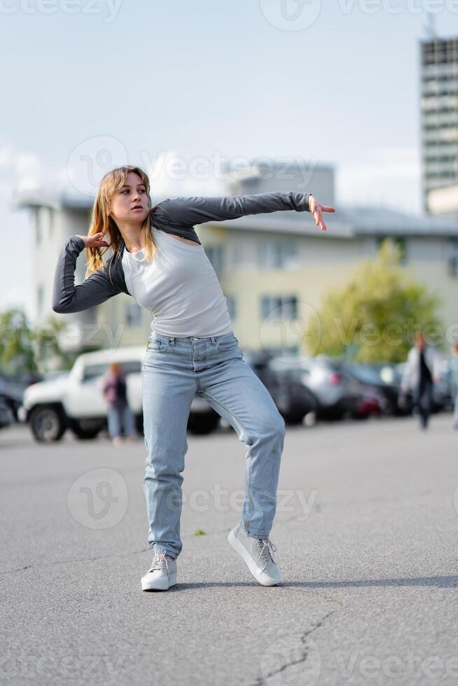 Young woman performs a dance move in a parking lot during daytime photo