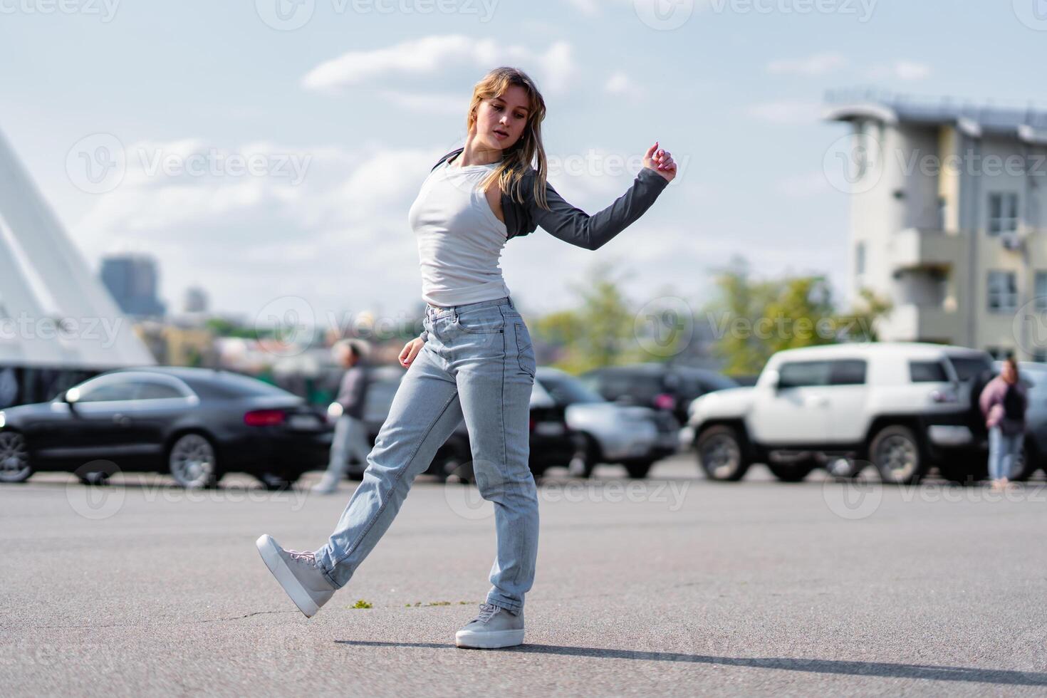 Young woman dancing in a parking lot on a sunny day with urban backdrop photo