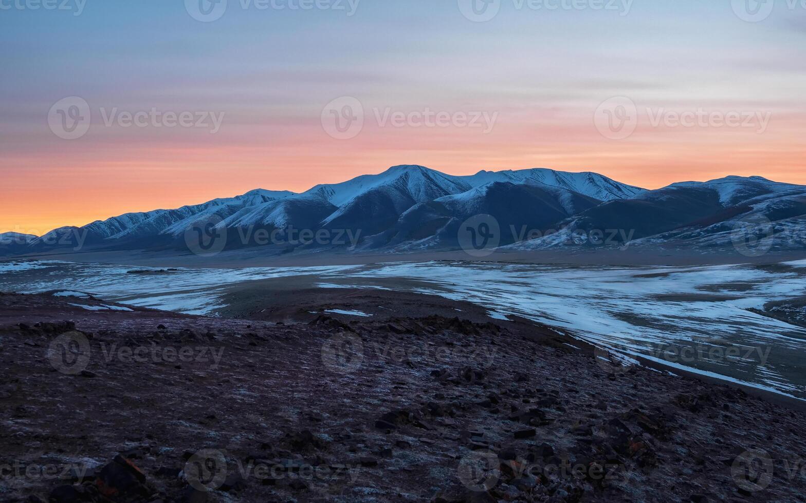 Panoramic mountain landscape with long snowy mountain range lit by dawn sun among low clouds. Awesome alpine scenery with high mountain ridge at sunset or at sunrise. Glacier on top in orange light. photo