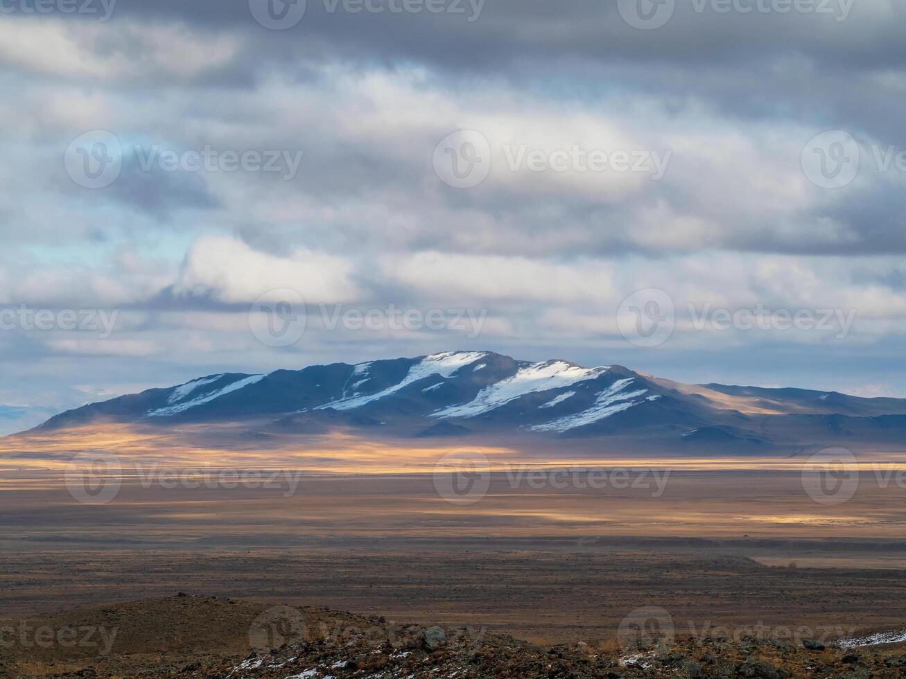 Withered grass field, snow covered mountains, cloudy sky. photo