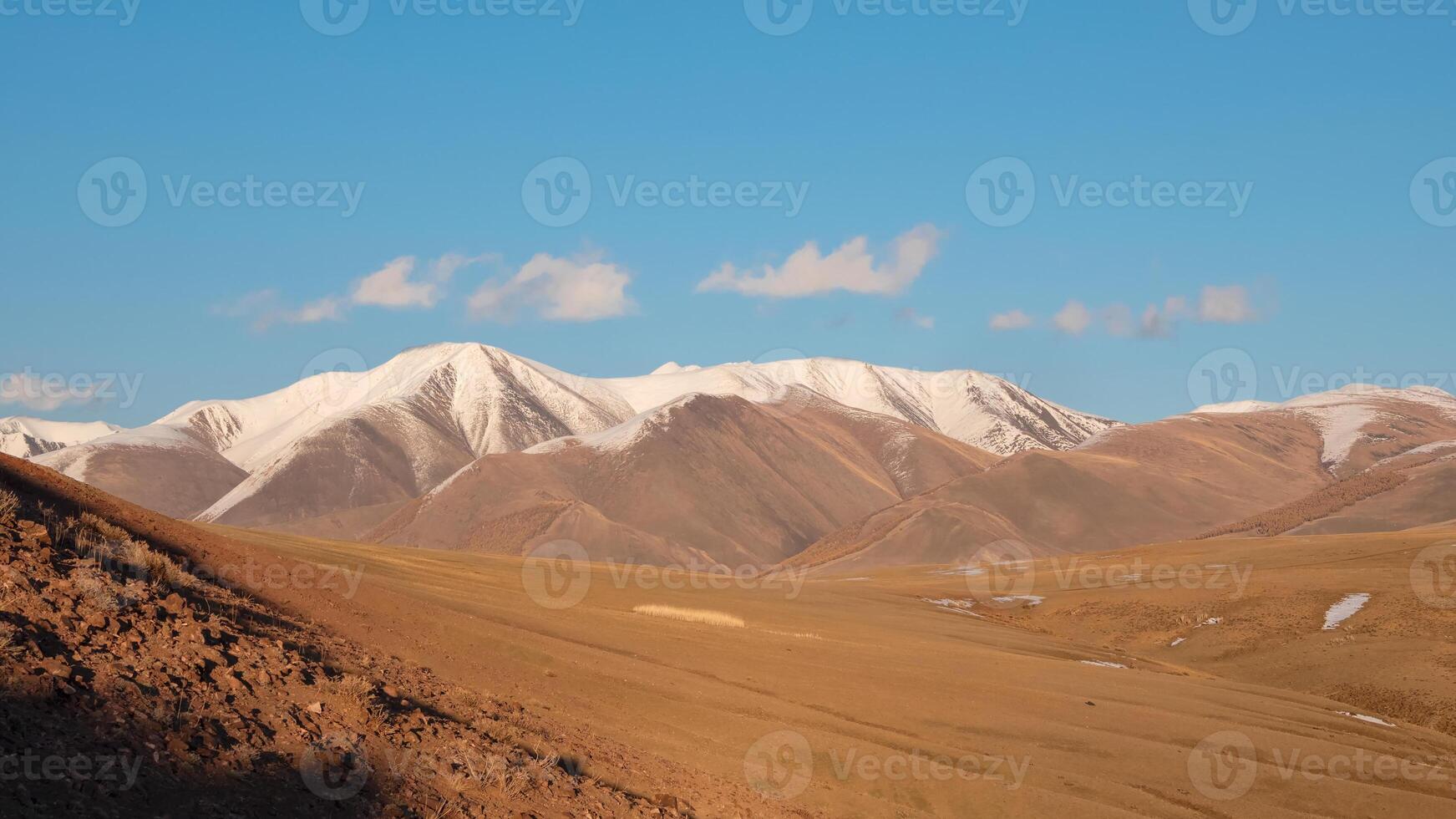 Wide panoramic view of bright autumn mountain steppe landscape. Awesome alpine view from pass to mountain valley in sunlight and great mountain silhouettes on horizon with white clouds on blue sky. photo