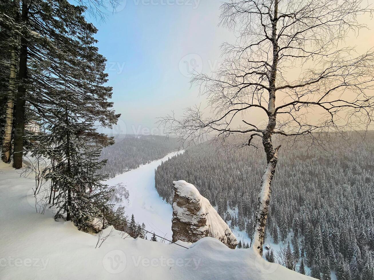Winter on the Usva pillars. Top view of a frozen river in a snowy wooded rocky canyon. photo