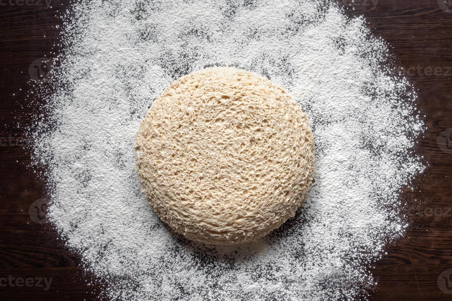 Round piece of yeast-free dough on a floured dark table. Cellular texture of yeast-free dough. White bread texture. Mankind oldest staple foods. Flat lay, copy space. photo