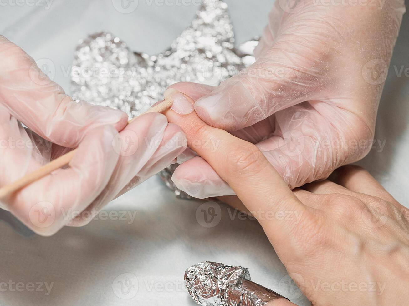 The manicurist removes the base coat from the nail with an orange stick during the manicure procedure at the Spa photo