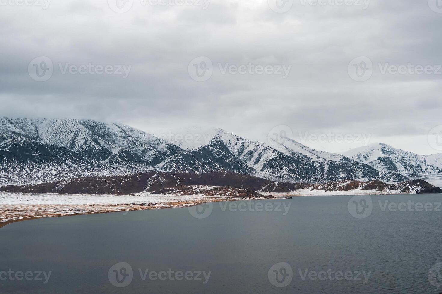 Snow-covered winter pastel colors landscape. View of the dark lake and snow hills. Cold winter weather. Harsh climate background in Mongolia. photo