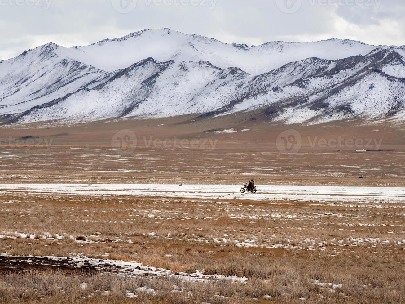 Beautiful Mongolian winter landscape snow mountain with a small figure of a ride on a black motorcycle through a wide snow-covered valley against the backdrop of high mountains. photo