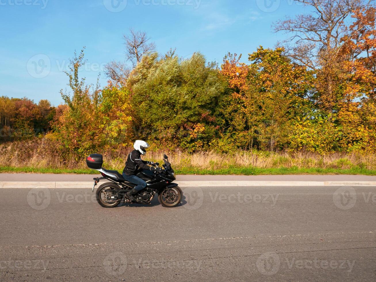 Motorcyclist in motion. Woman biker on a black motorcycle in traffic on a rural autumn road. photo