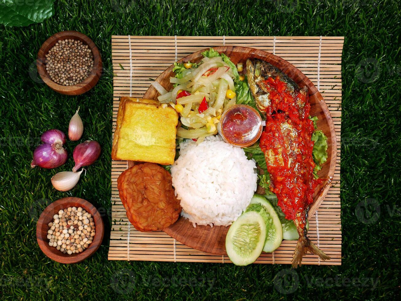 Top view, complete Mixed Rice served with white rice, sambal fish, tempeh, tofu, fresh vegetables, sambal, and spices on a bamboo mat. photo