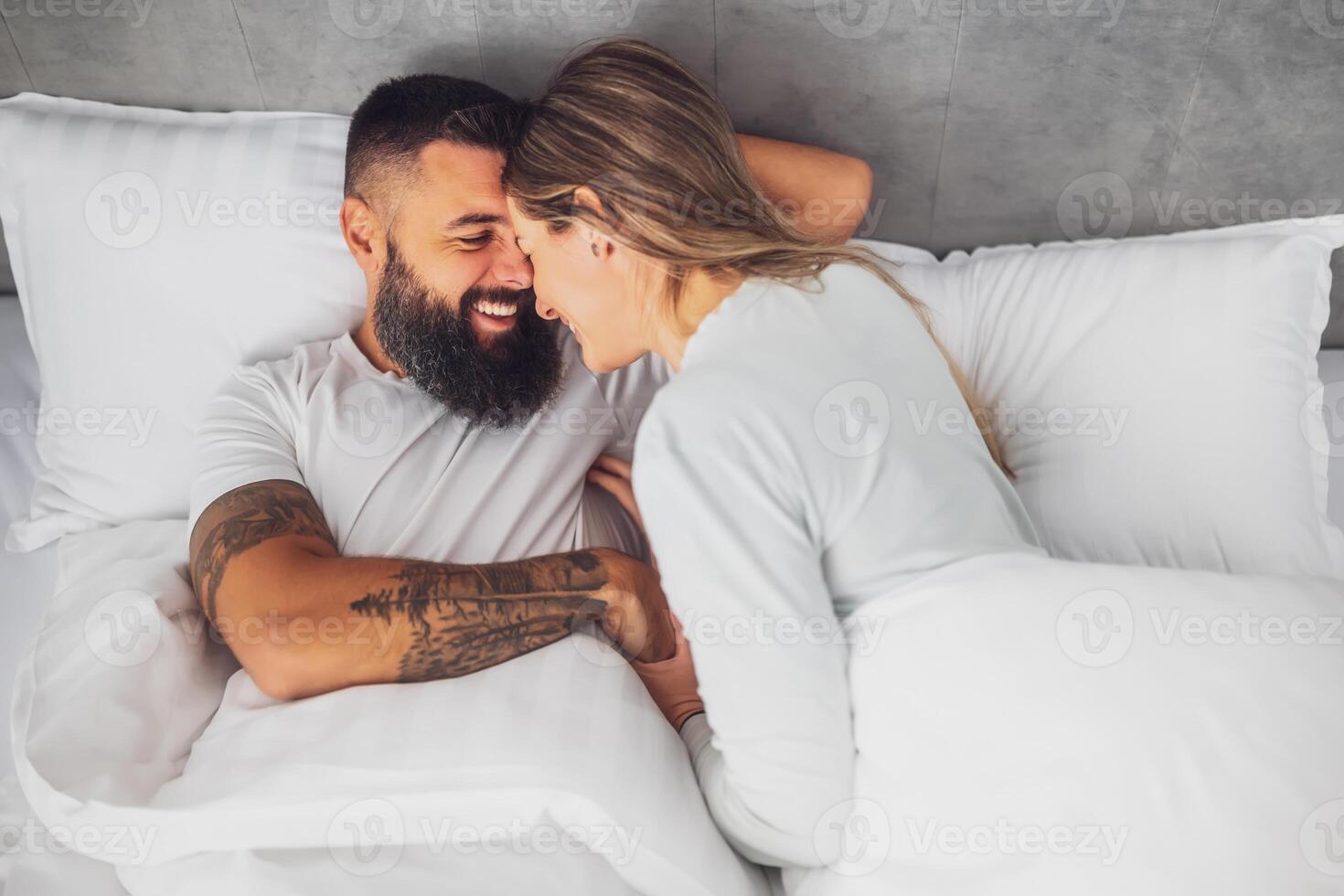 Happy loving couple is lying in bed in the morning. They are relaxing and smiling. photo