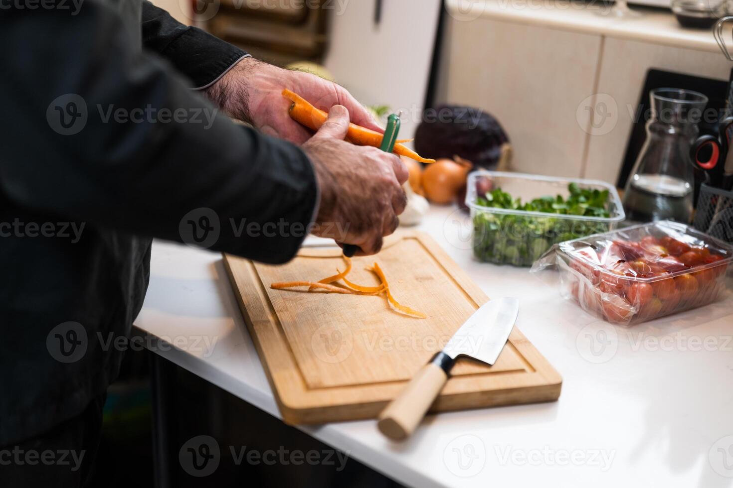 Close up of professional chef preparing ingredients for vegetarian meal in restaurant's kitchen. He is scraping carrot. photo