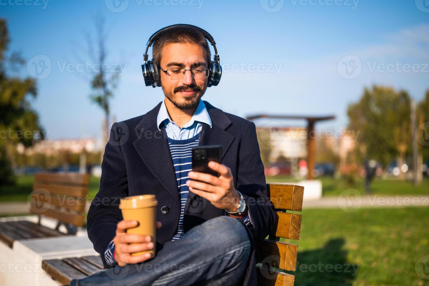 Businessman using headphones and mobile phone while drinking coffee outdoor. photo