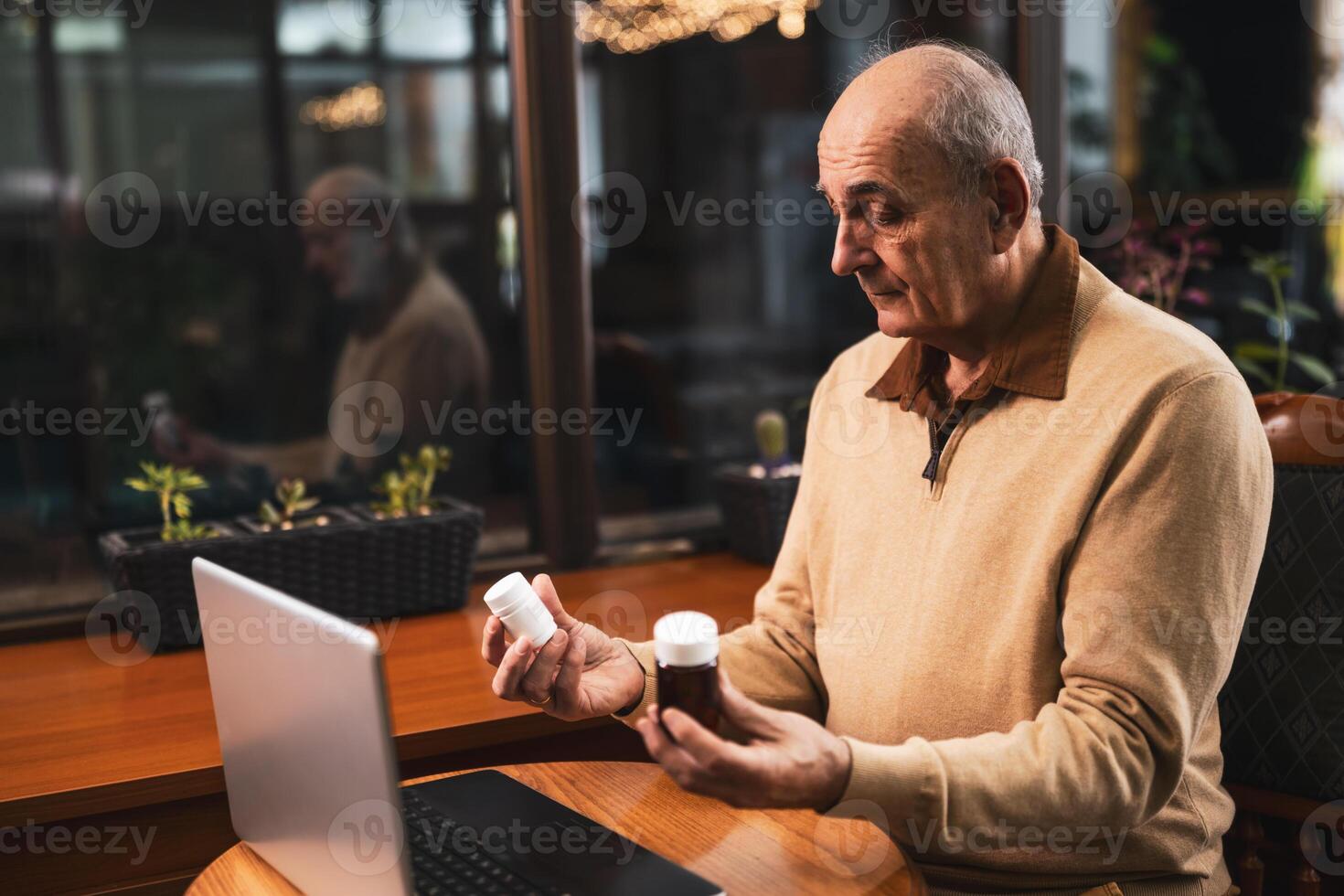 Uncertain senior man having online consultation with his doctor on laptop while showing him two bottle of pills. He is asking for advice for his health problems while sitting in the cafe. photo