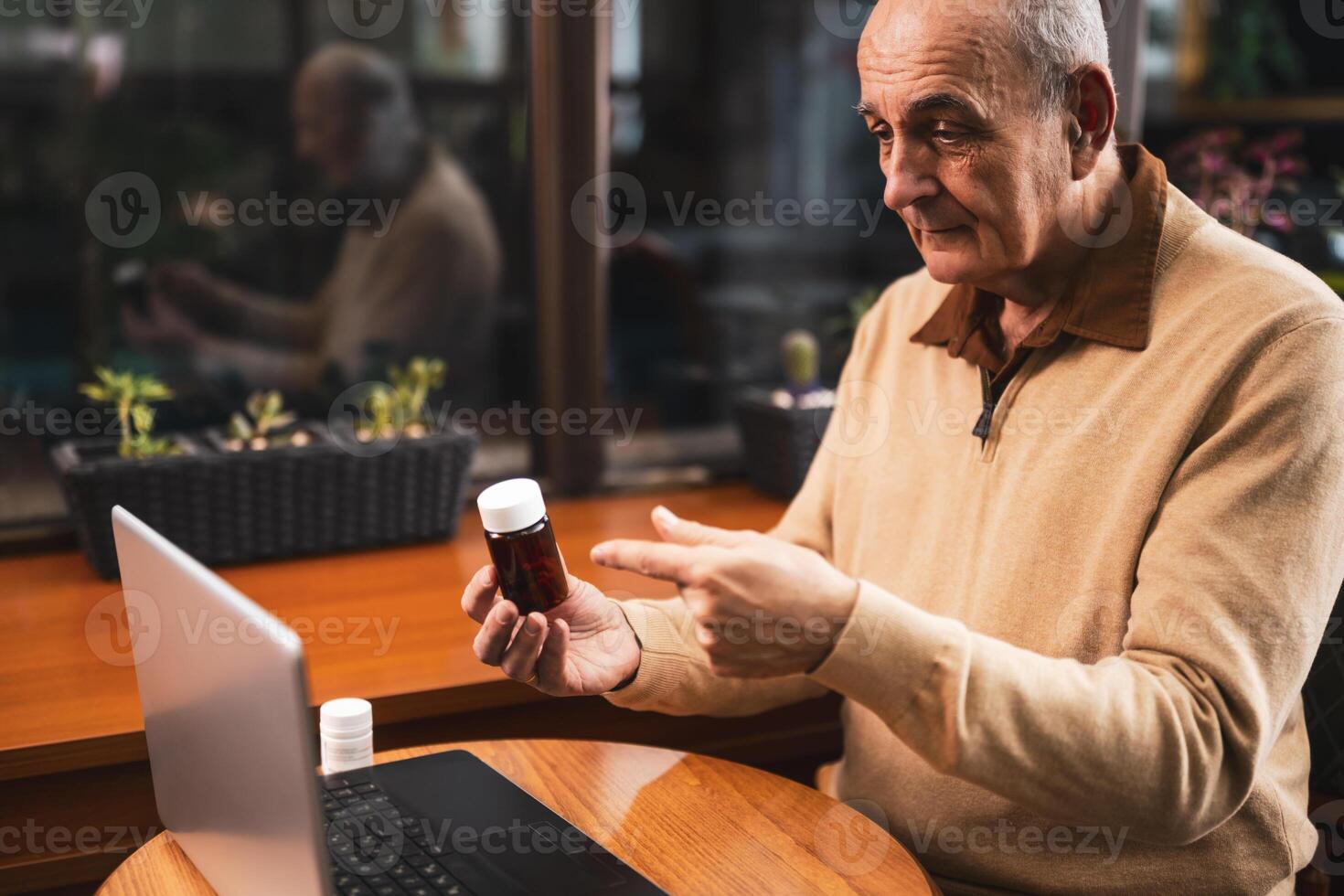 Senior man showing bottle of pills and talking with his doctor during a call on laptop while sitting in the city cafe photo
