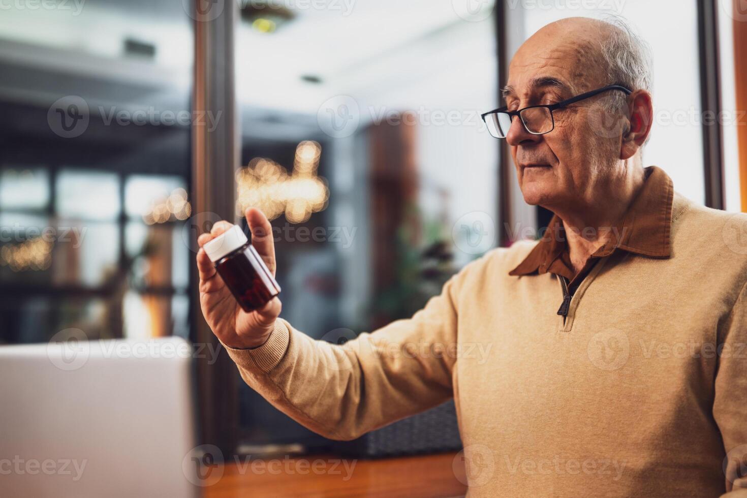 Senior man with eyeglasses holding bottle of pill and using laptop while sitting in the cafe. photo