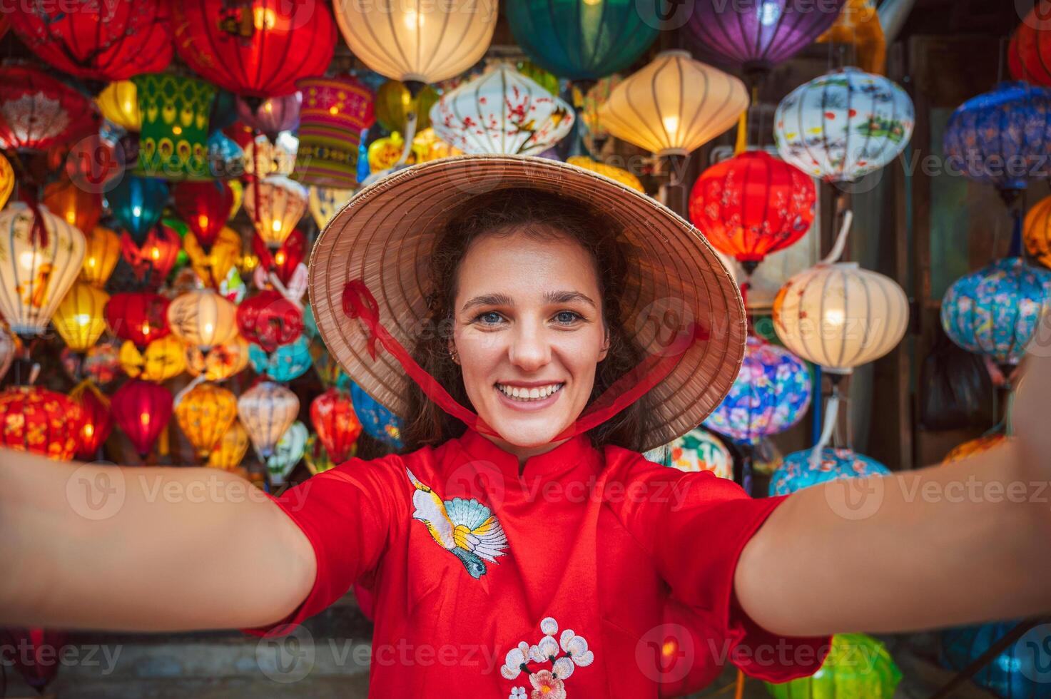 Selfie of a woman in traditional Vietnamese clothes and a conical Non La hat against the background of lanterns in the ancient city of Hoi An. photo