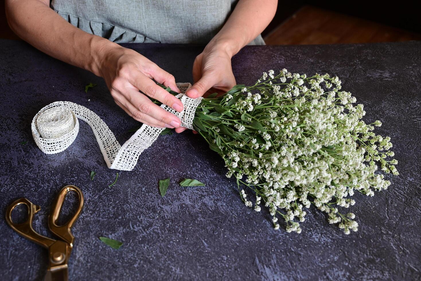 The photograph provides a close-up view of hands tying a white lace ribbon around a bouquet of delicate white flowers. photo