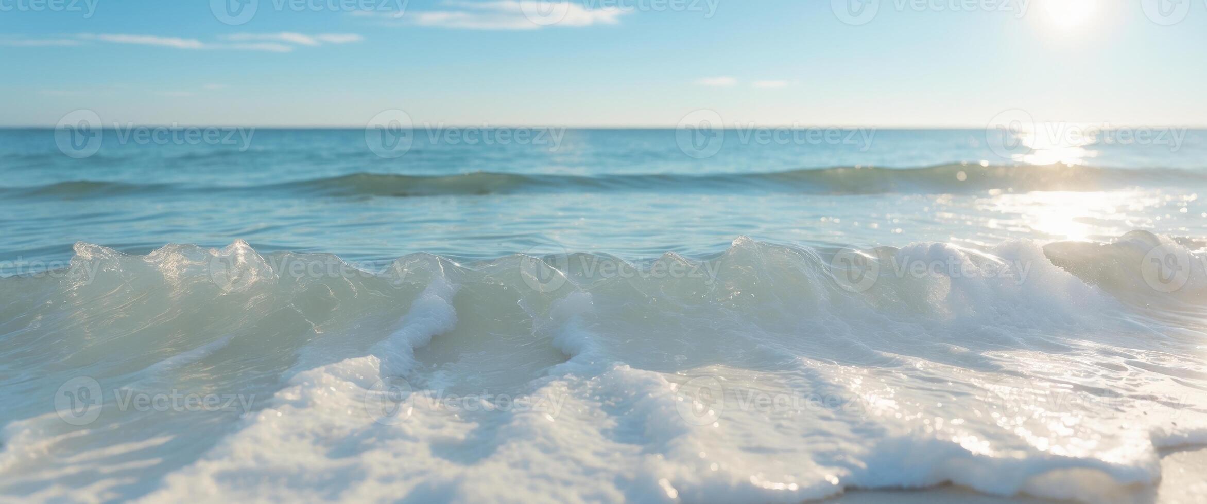 A wave is seen on the beach with the sun shining photo
