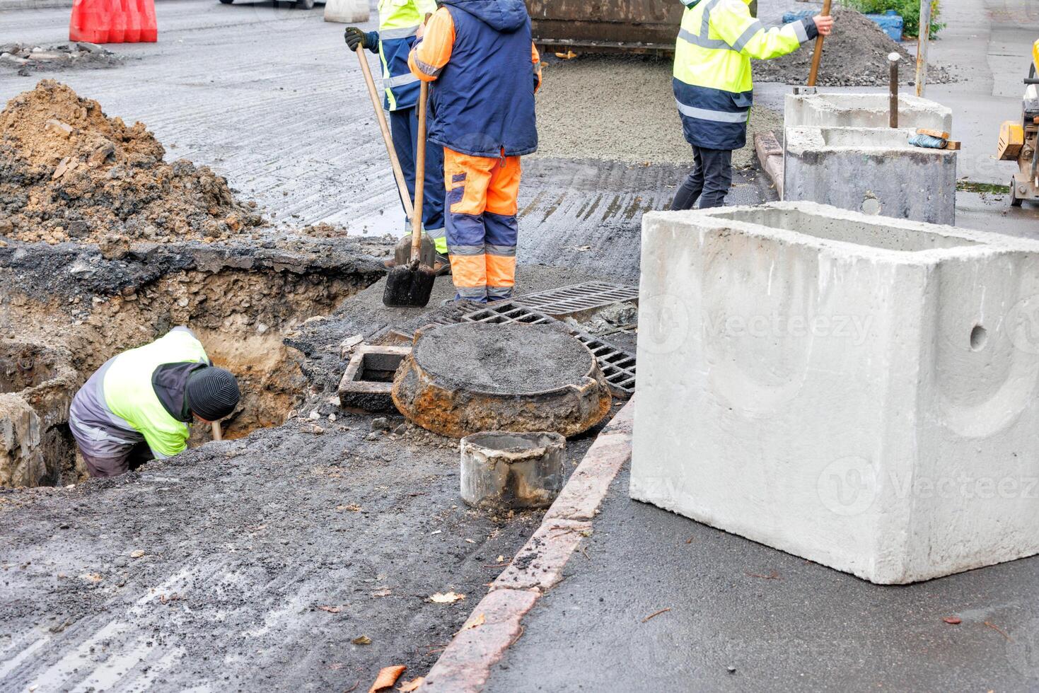 A group of road workers repair sewer storm hatches on a roadway on an autumn day. photo