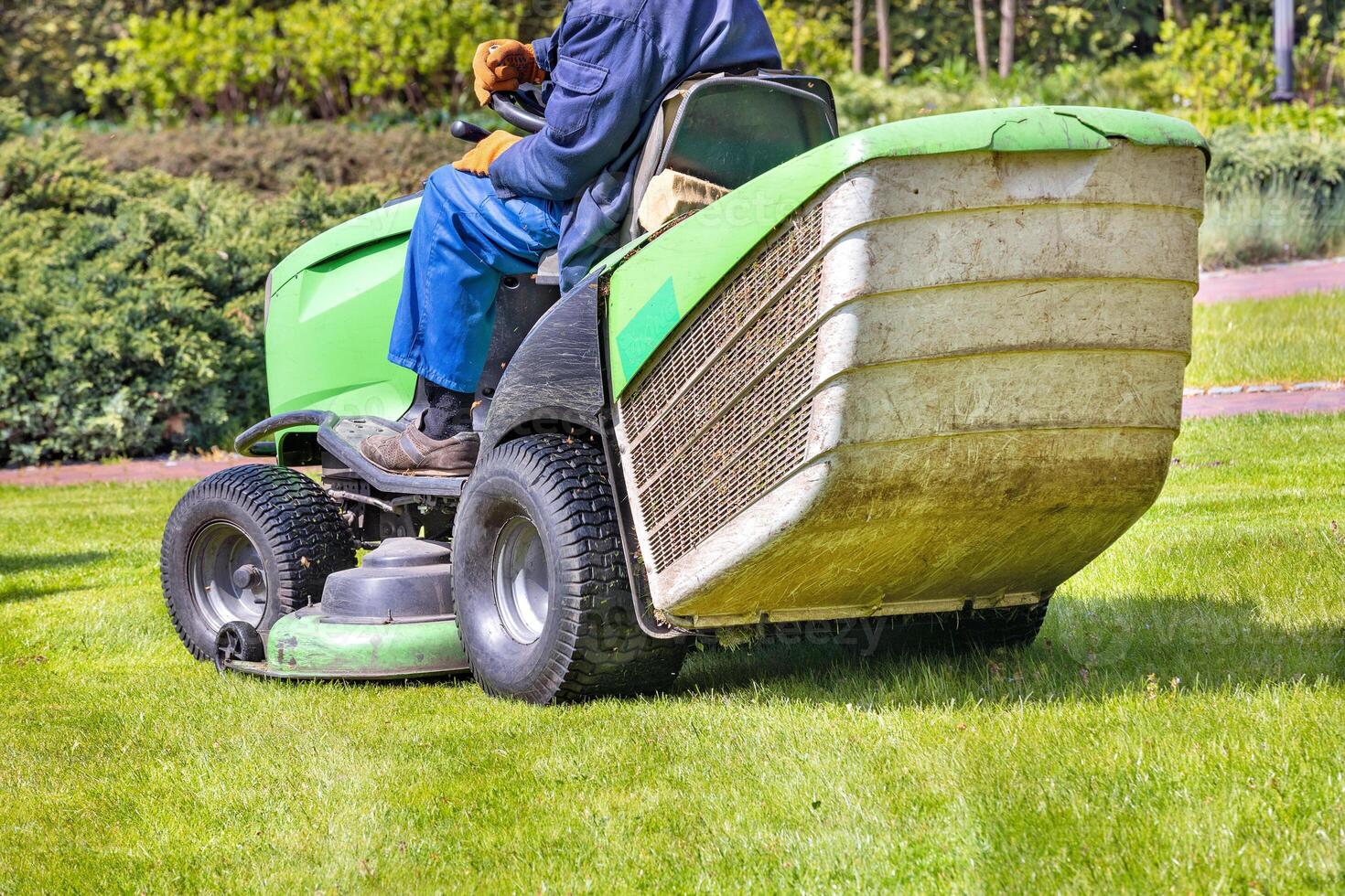 A gardener mows a green lawn while riding a tractor lawn mower on a bright spring day. photo