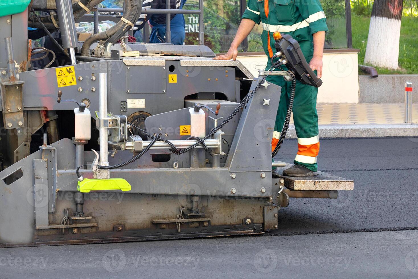 A fragment of the work of an industrial asphalt paver, an engineer stands on the footboard and controls the process. photo