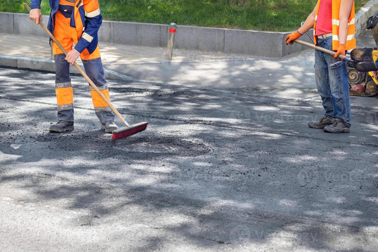 A road maintenance workers cleans up the new asphalt pavement on the carriageway with a brush and shovel. photo