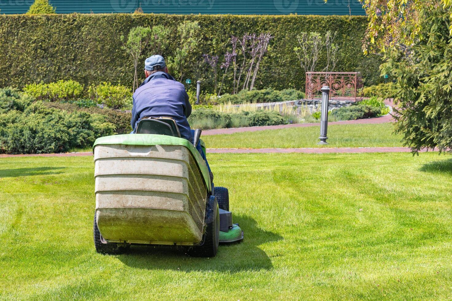 A gardener takes care of a green lawn by cutting the grass while riding a tractor lawn mower on a bright spring day. photo