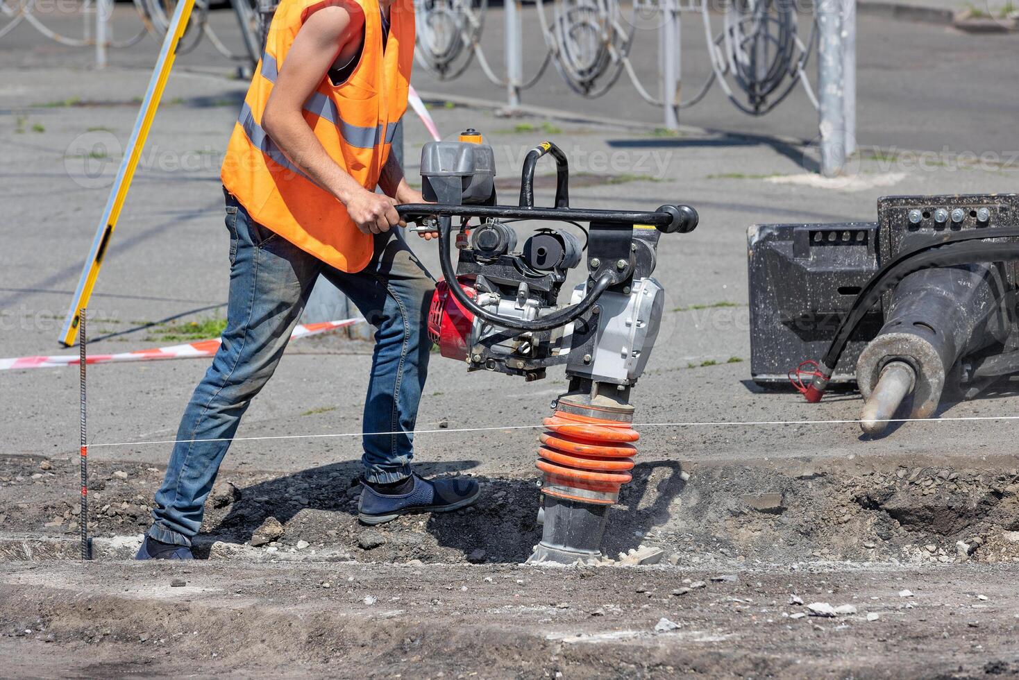 A construction worker is ramming a trench with a vibrating rammer at a construction site on a sunny summer day. photo