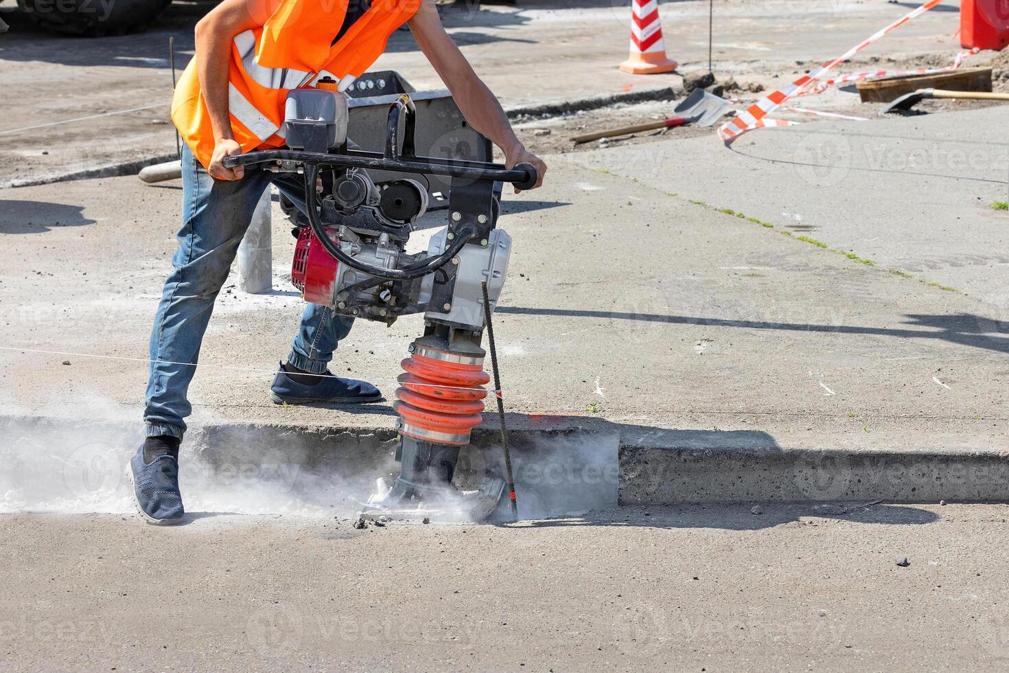 A construction worker is ramming a trench with a vibrating rammer at a construction site and kicking up a cloud of dust around him. photo