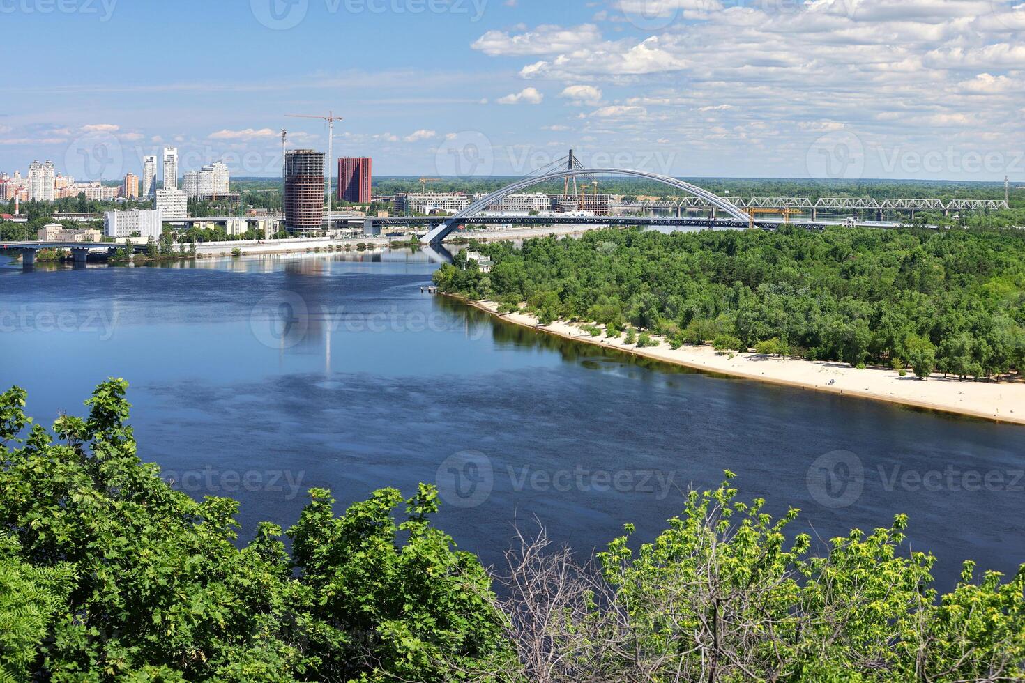Aerial view of the breathtaking summer skyline of Kyiv from a bird's eye view overlooking the green park, sandy beach, bridges and city buildings. photo