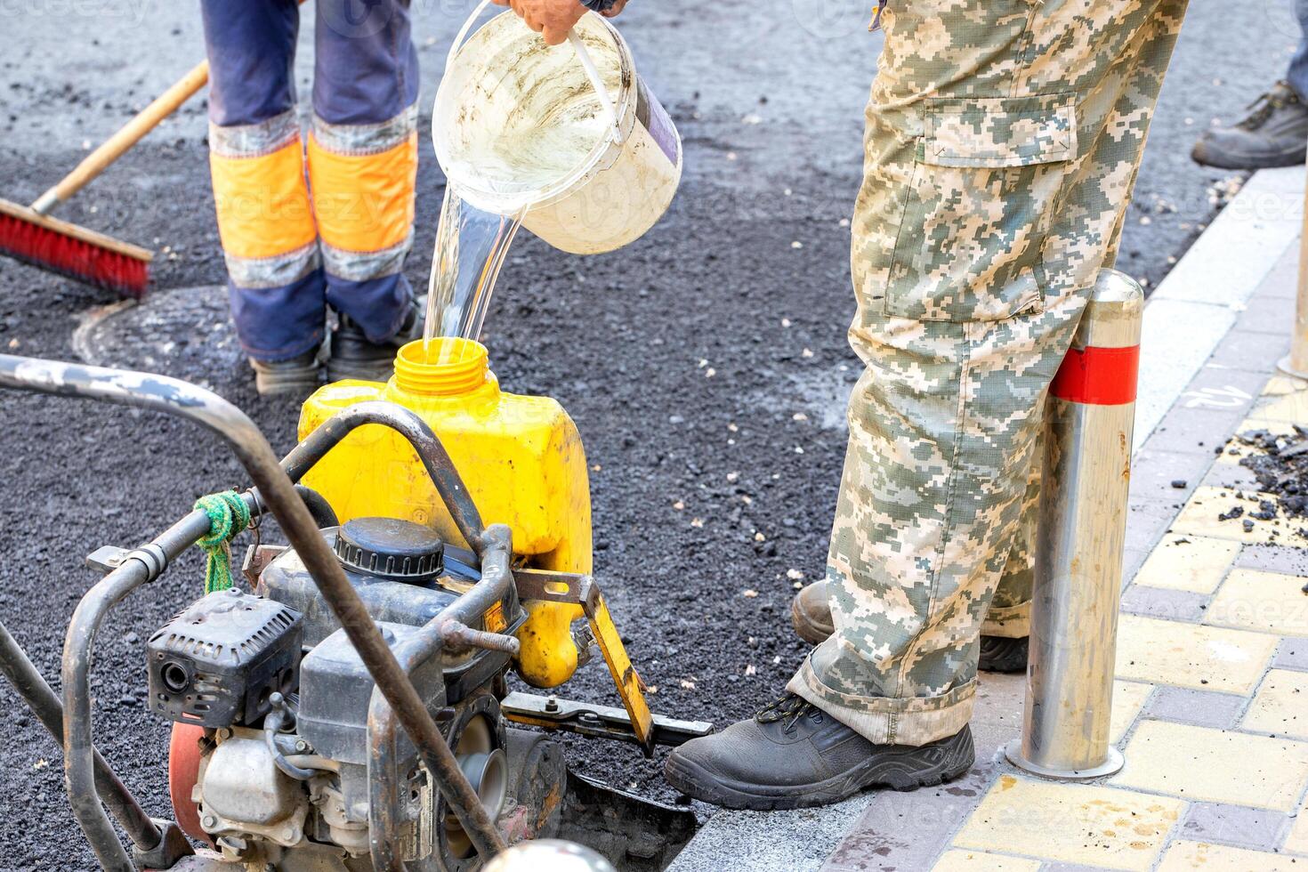 A worker fills the plastic tank of an old compact plate with water at a work site. photo