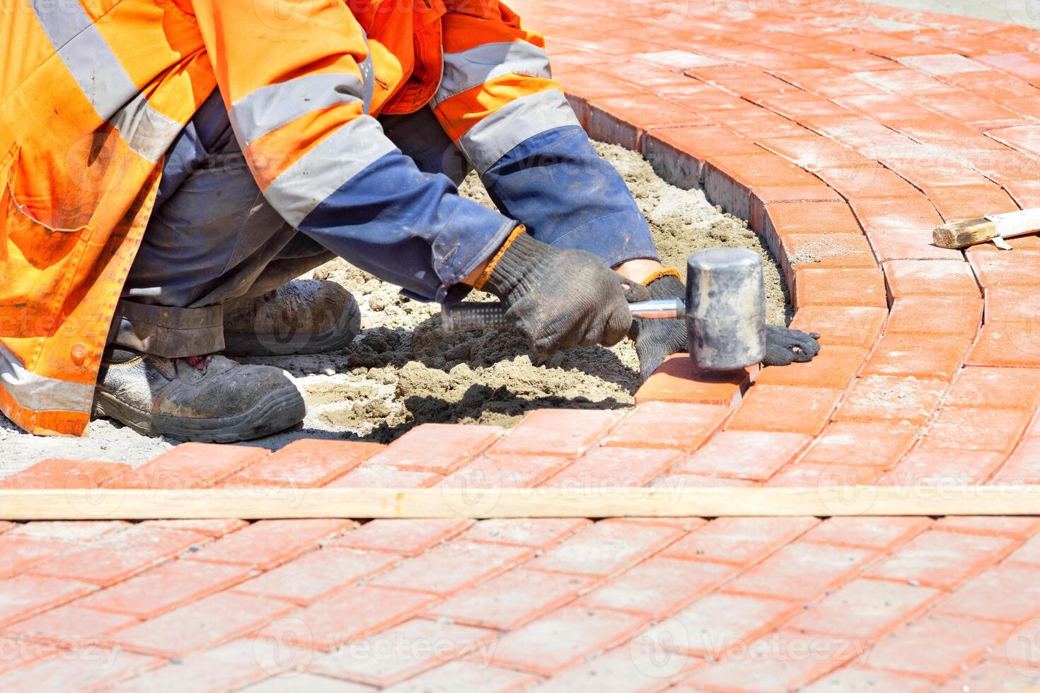 A squatting worker lays paving slabs by a wooden level on a sunny summer day. photo