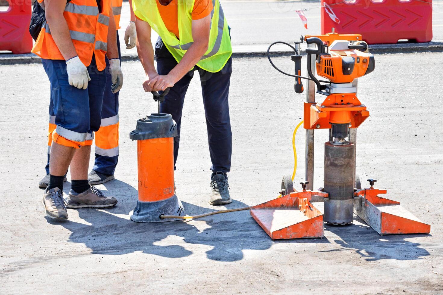 Road workers in reflective raincoats drill asphalt with a core drill. photo