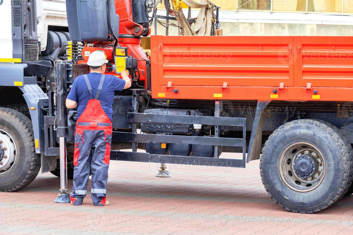 The driver of a truck with a hydraulic manipulator examines and adjusts the operation of the lifting mechanism. photo