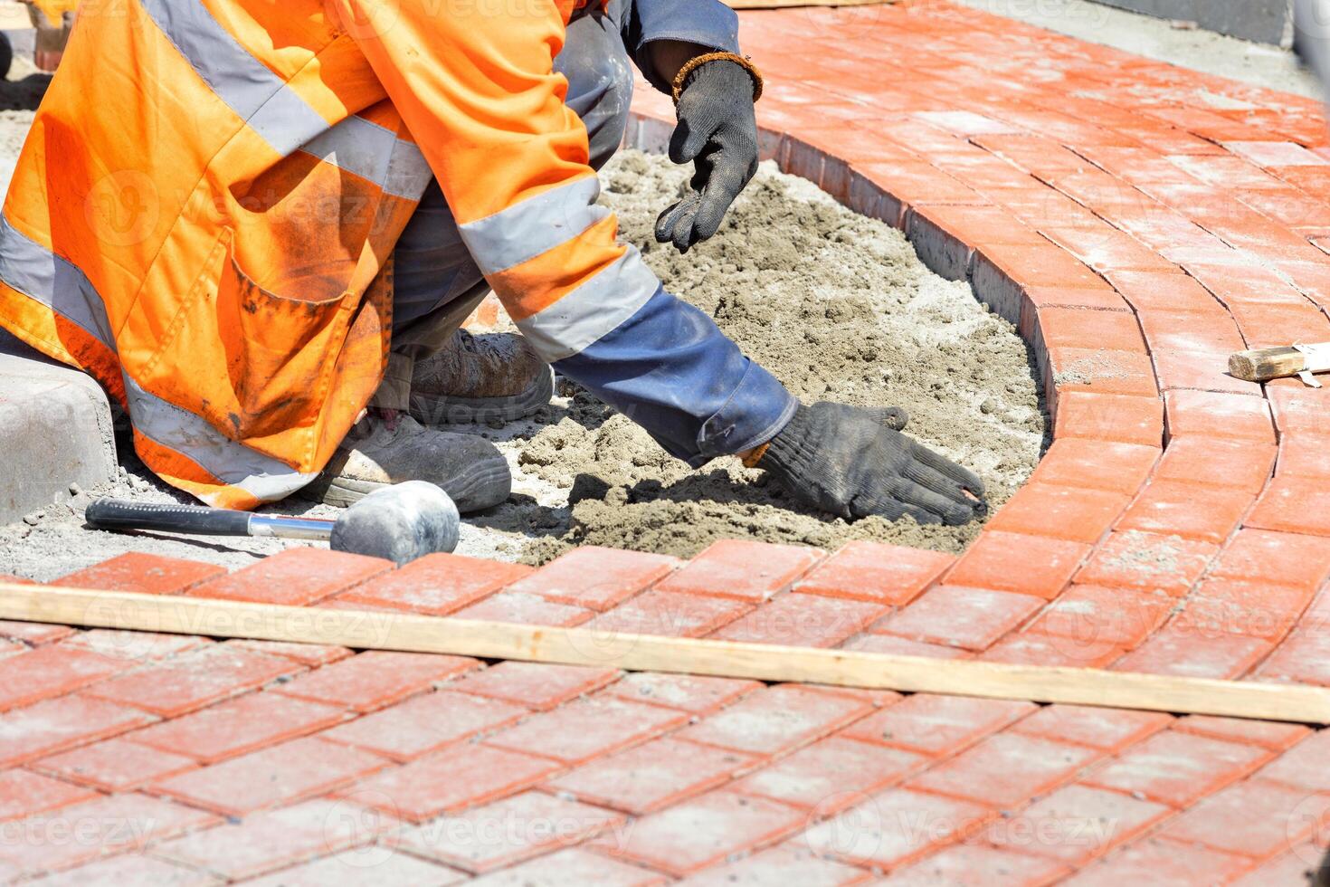 A master mason lays orange paving slabs around a traffic circle on the road. photo