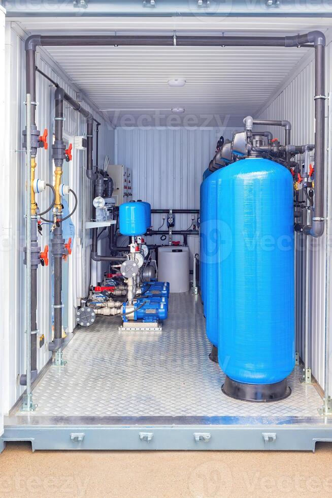 Industrial water filtration system inside container with blue tanks, pipes, machinery, valves, clean water solution. photo