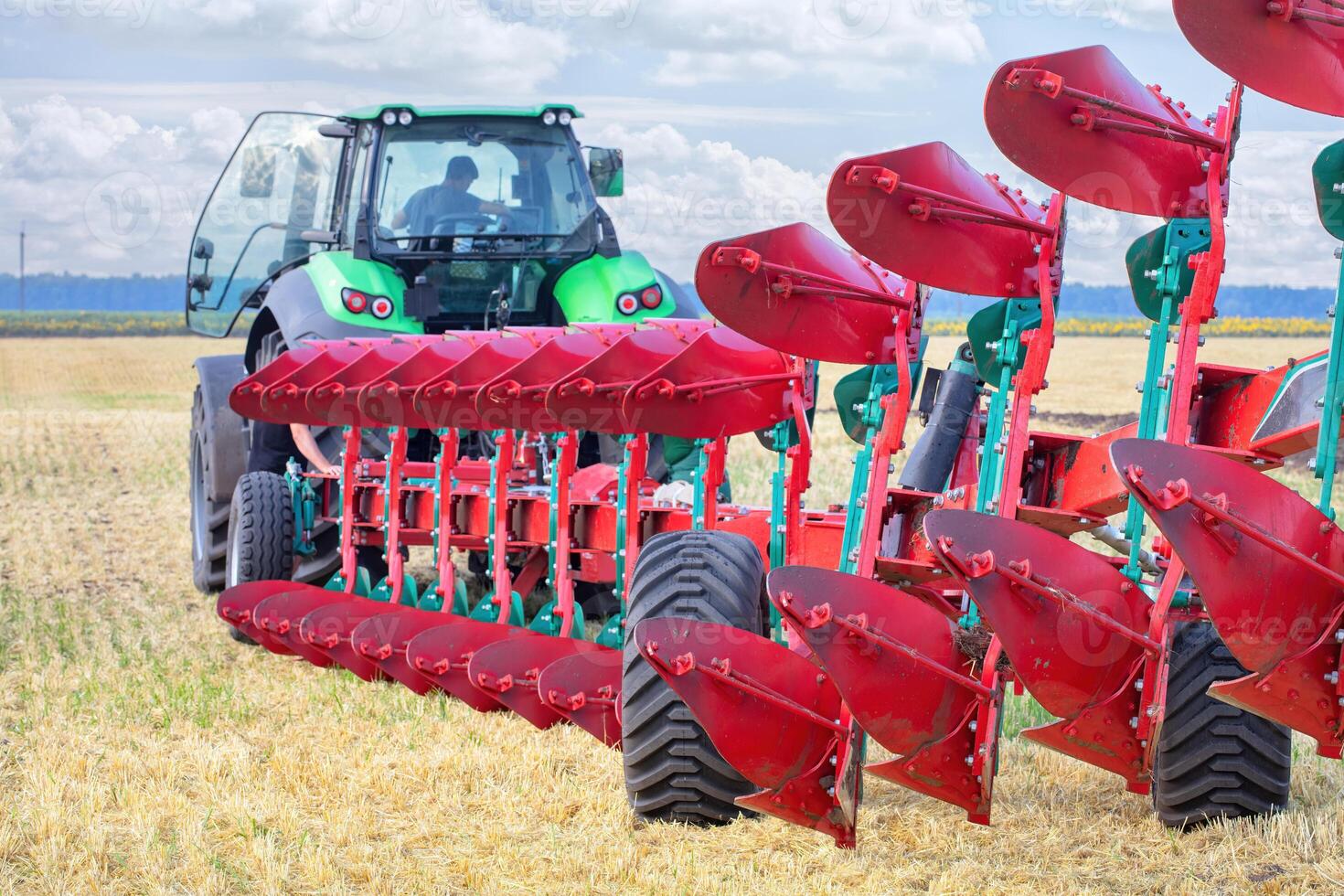 Modern farming with a green tractor and red plow in a vast agricultural field during daylight photo