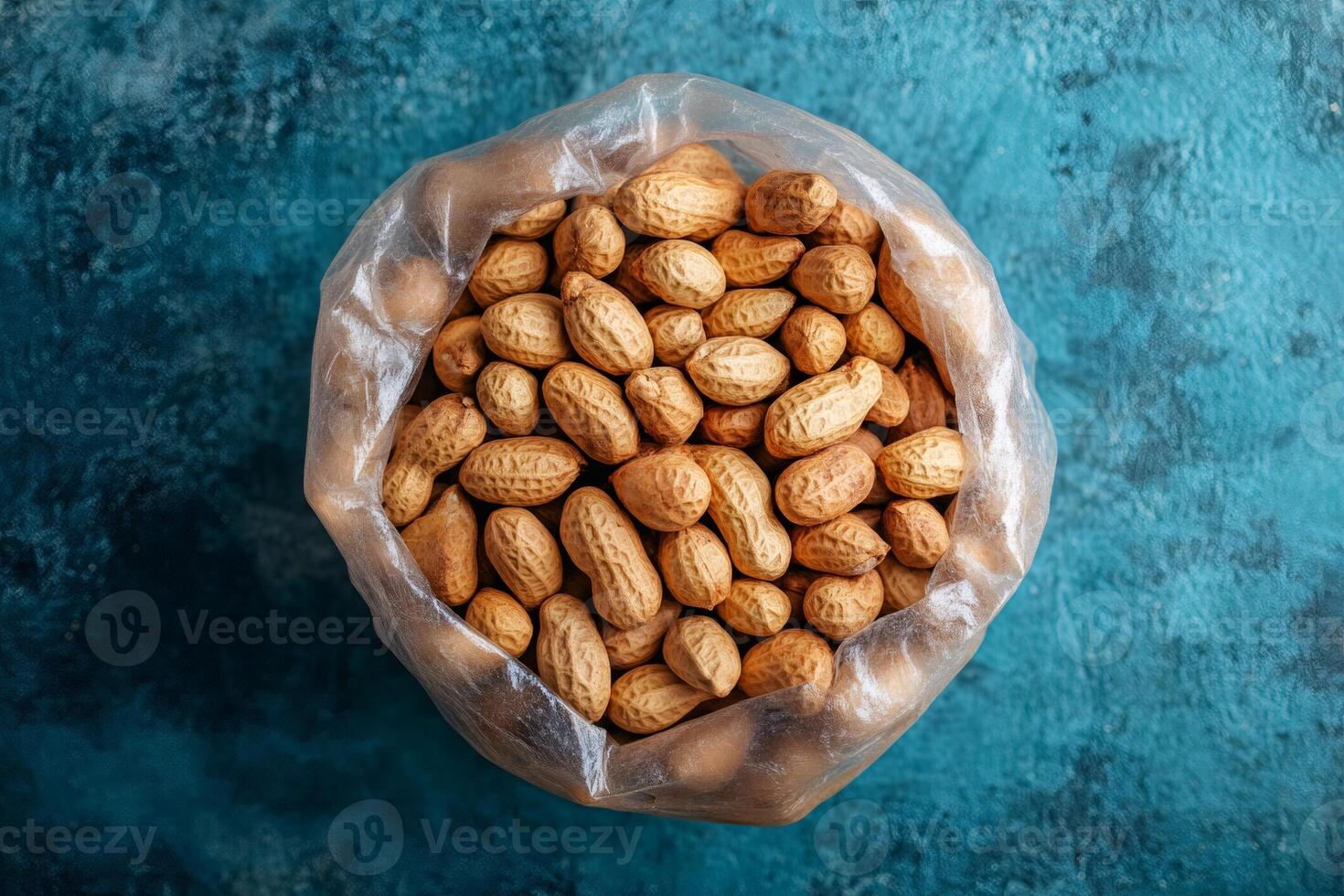 Peanuts in shell filling transparent plastic bag on rustic turquoise background photo