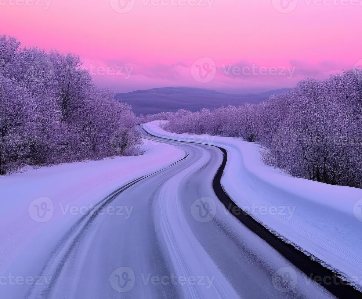 Winding road through snowy landscape at dawn with pink sky photo