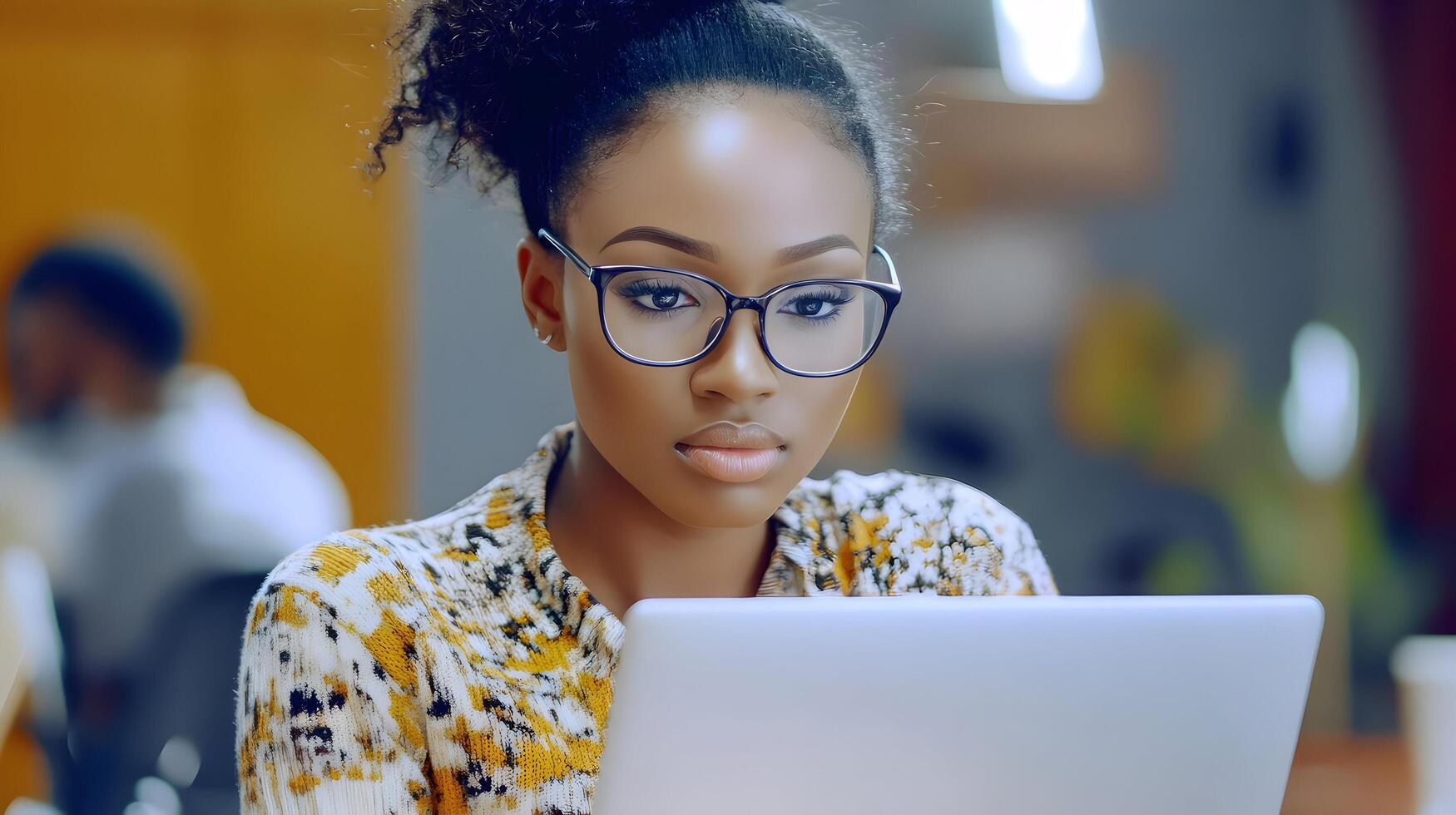 Portrait of a young,intelligent and ambitious African American woman wearing glasses and using a laptop computer in a modern office setting. She is working on a digital device,researching. photo