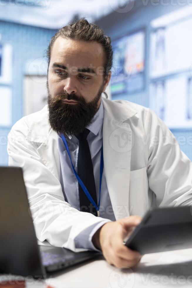 General practitioner working with healthcare records and test results to find the diagnosis in his office, examining x rays and reports. Doctor doing research for disease prevention and treatment. photo