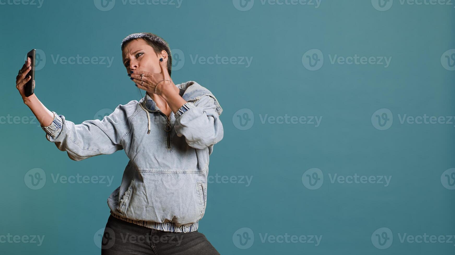 Silly confident woman recording a while she shows groovy dance moves, filming on her smartphone and fooling around in studio. Funky bold edgy person being funny. Camera B. photo