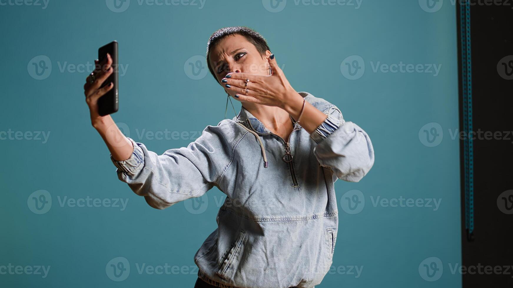Silly confident woman recording a while she shows groovy dance moves, filming on her smartphone and fooling around in studio. Funky bold edgy person being funny. Camera A. photo
